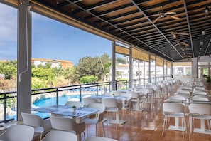 En restaurant med udendørs siddepladser med udsigt over en pool og grøn bevoksning.
