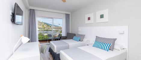 A hotel room with two beds, a balcony with chairs, a TV, and a ceiling fan.