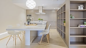 Una cocina moderna con una isla central, sillas blancas y una estantería empotrada.