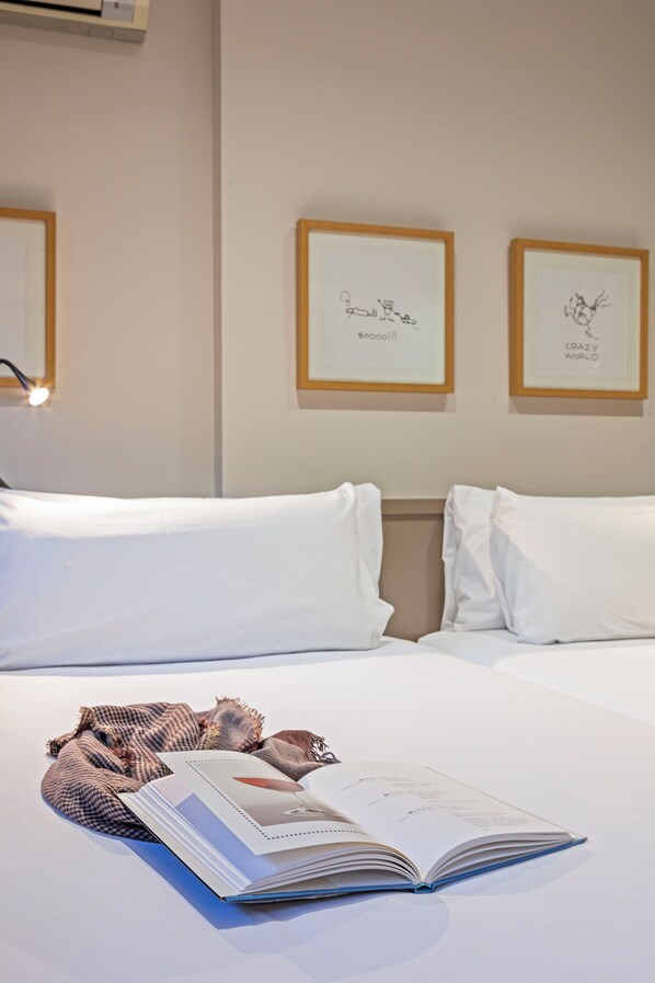 A hotel room with a neatly made bed, a book on the bed, and two framed pictures on the wall.