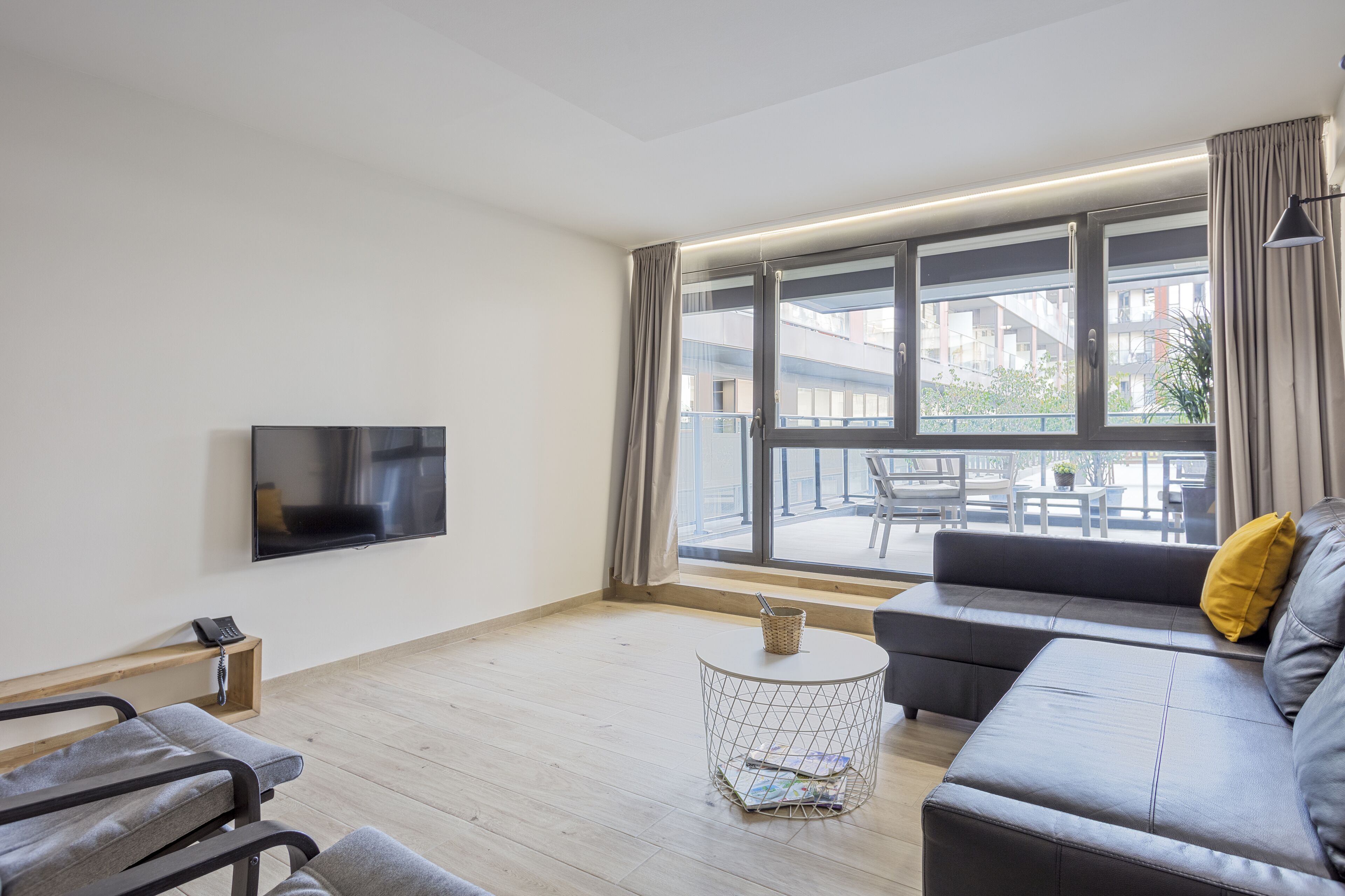 Una sala de estar moderna con un sofá, una mesita redonda, un televisor y vistas al balcón.