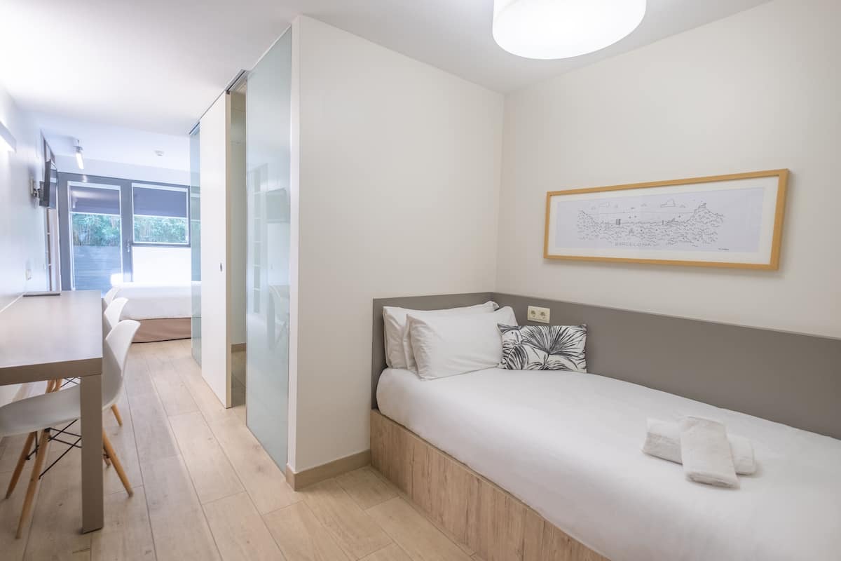 A modern bedroom with a bed, a desk, and a chair. There is a framed picture on the wall.