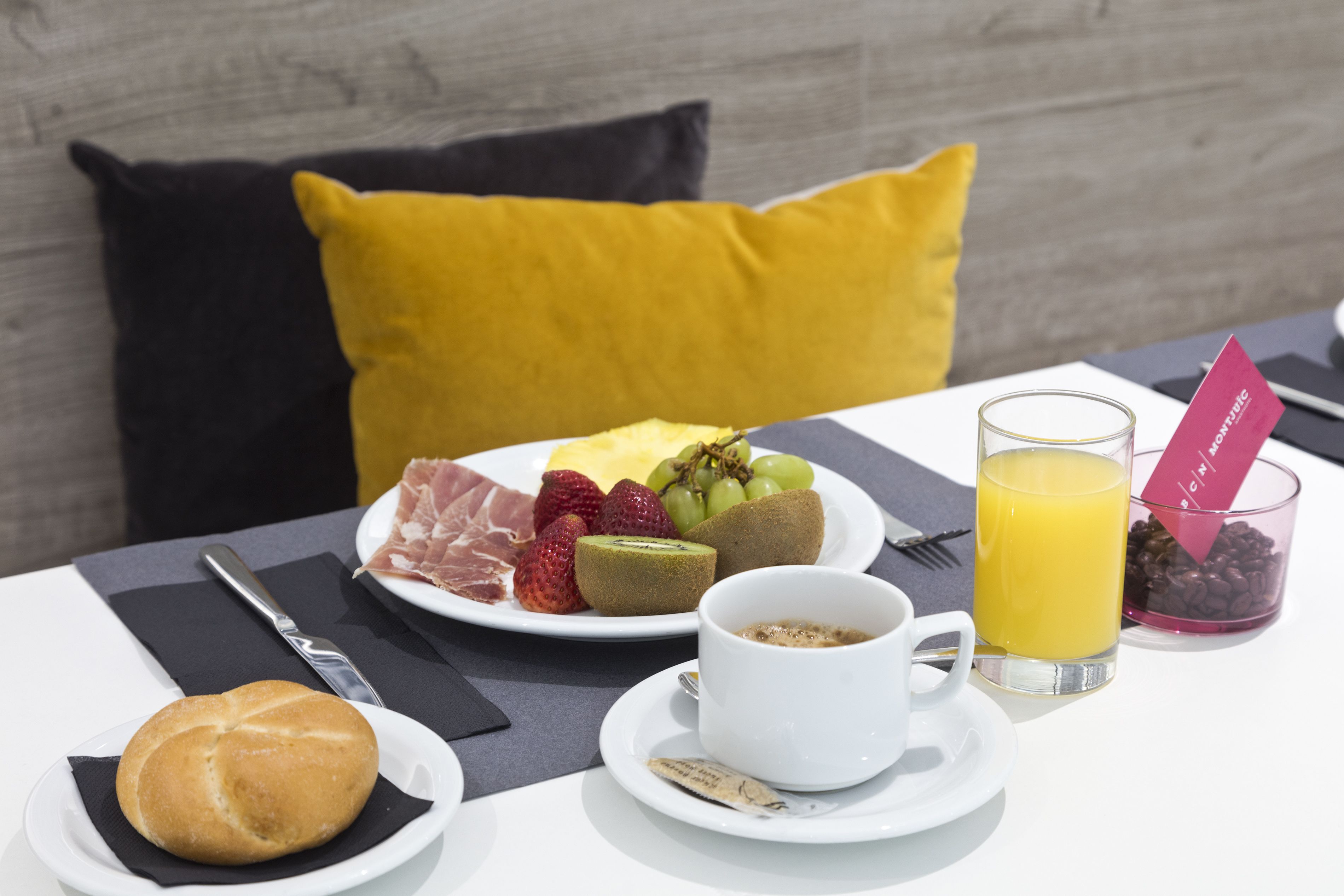 A breakfast setting with a plate of fruits, a glass of orange juice, a cup of coffee, and a small bowl of coffee beans.