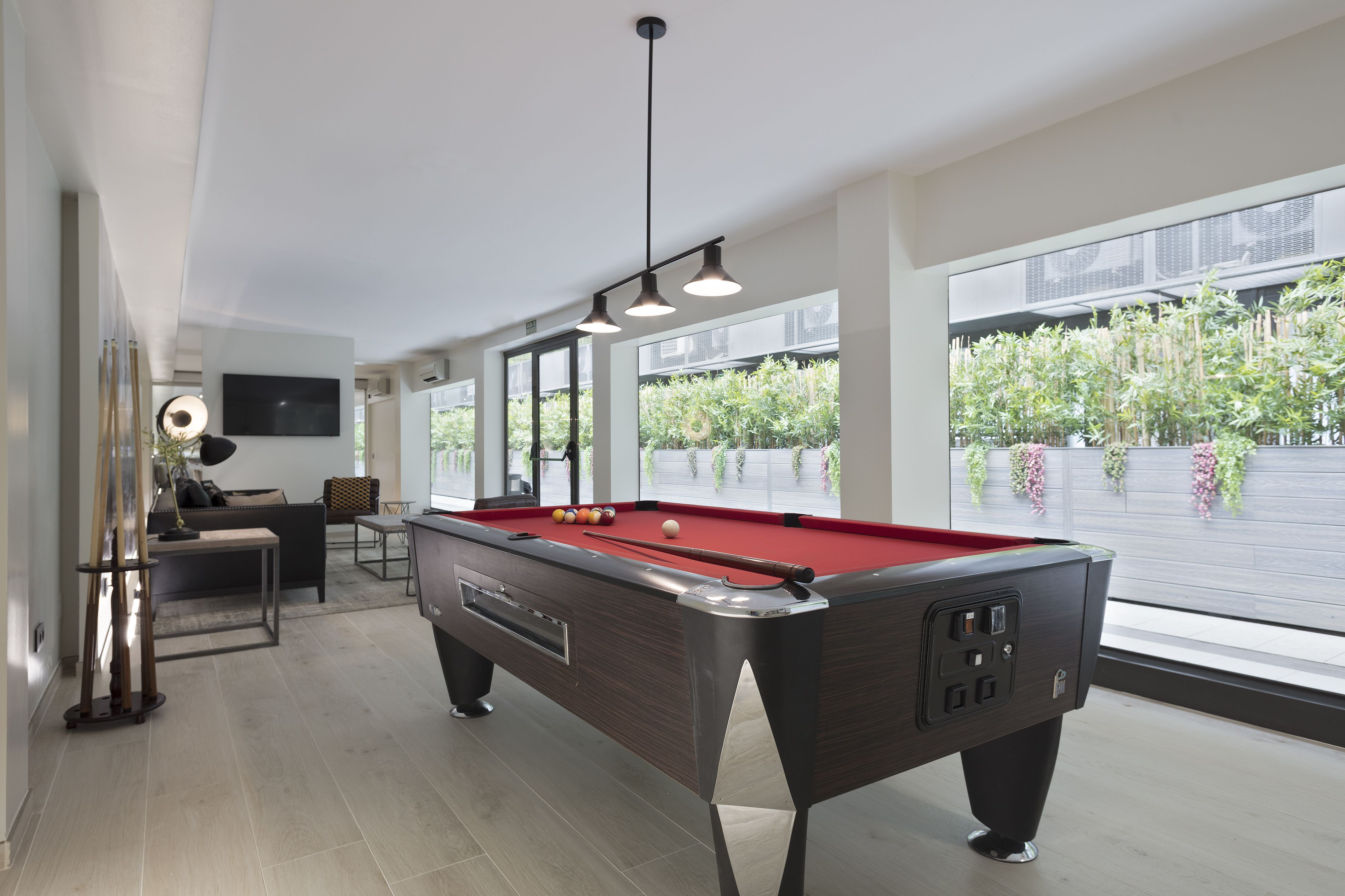A modern pool table in a well-lit room with large windows, a sofa, and a television.