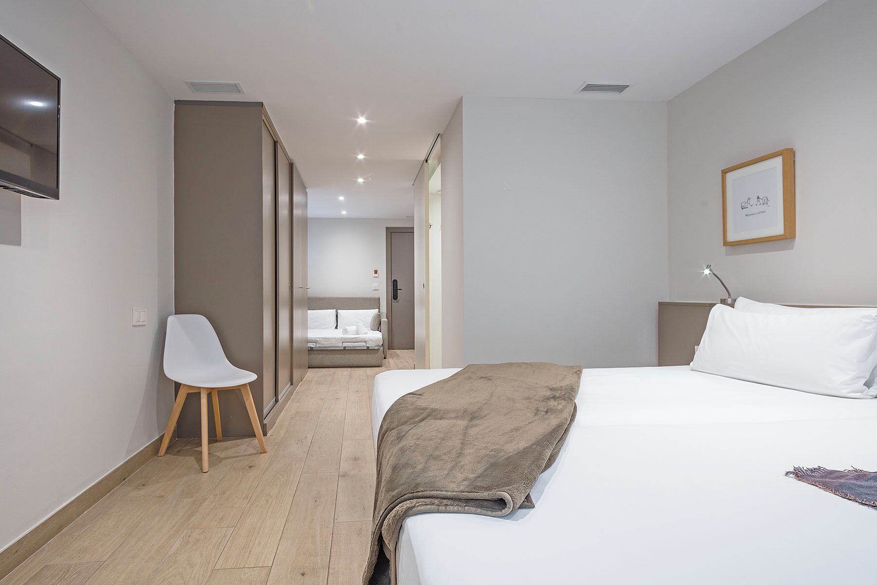 Ein modernes Hotelzimmer mit einem großen Bett, einem Nachttisch, einem Sessel und Blick auf die Empfangshalle.