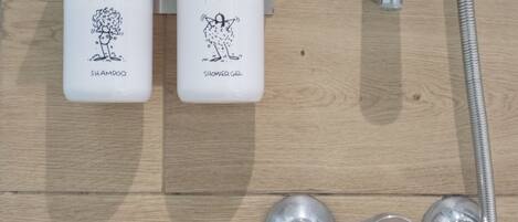 A shower area with two bottles of Montjuic shampoo and shower gel, a handheld showerhead, and a flexible hose.