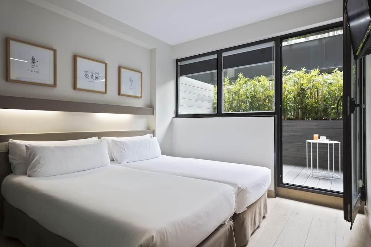 Un dormitorio moderno con una cama grande, un ventanal corredero a un balcón y cuadros en la pared.