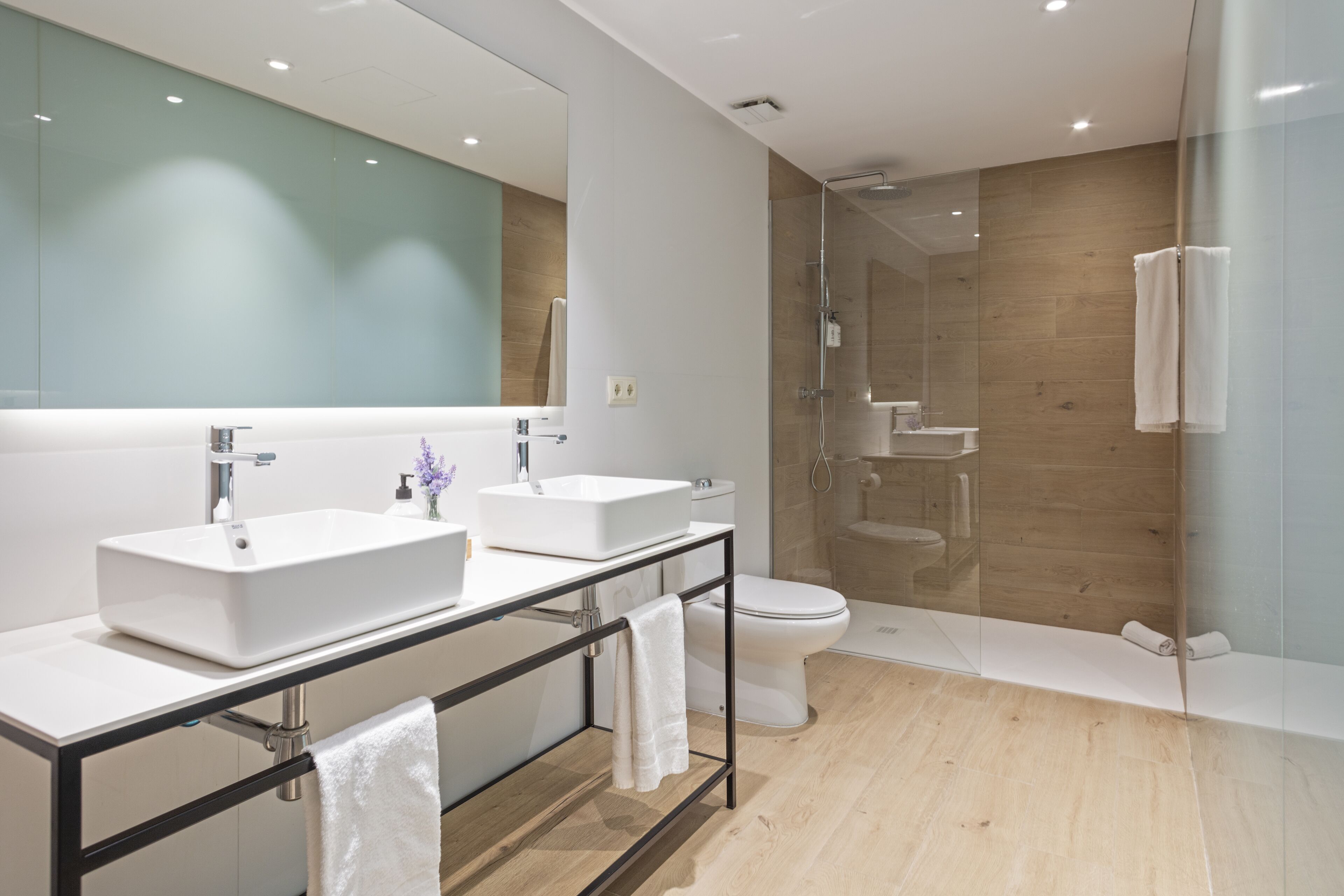 Un baño moderno con dos lavamanos, inodoro y zona de ducha con mampara de vidrio.
