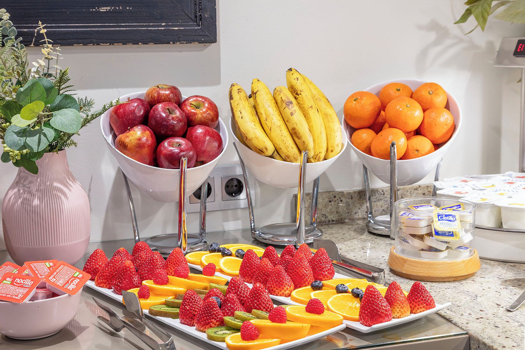 A buffet with bowls of apples, bananas, and oranges, and a tray of assorted fruits.