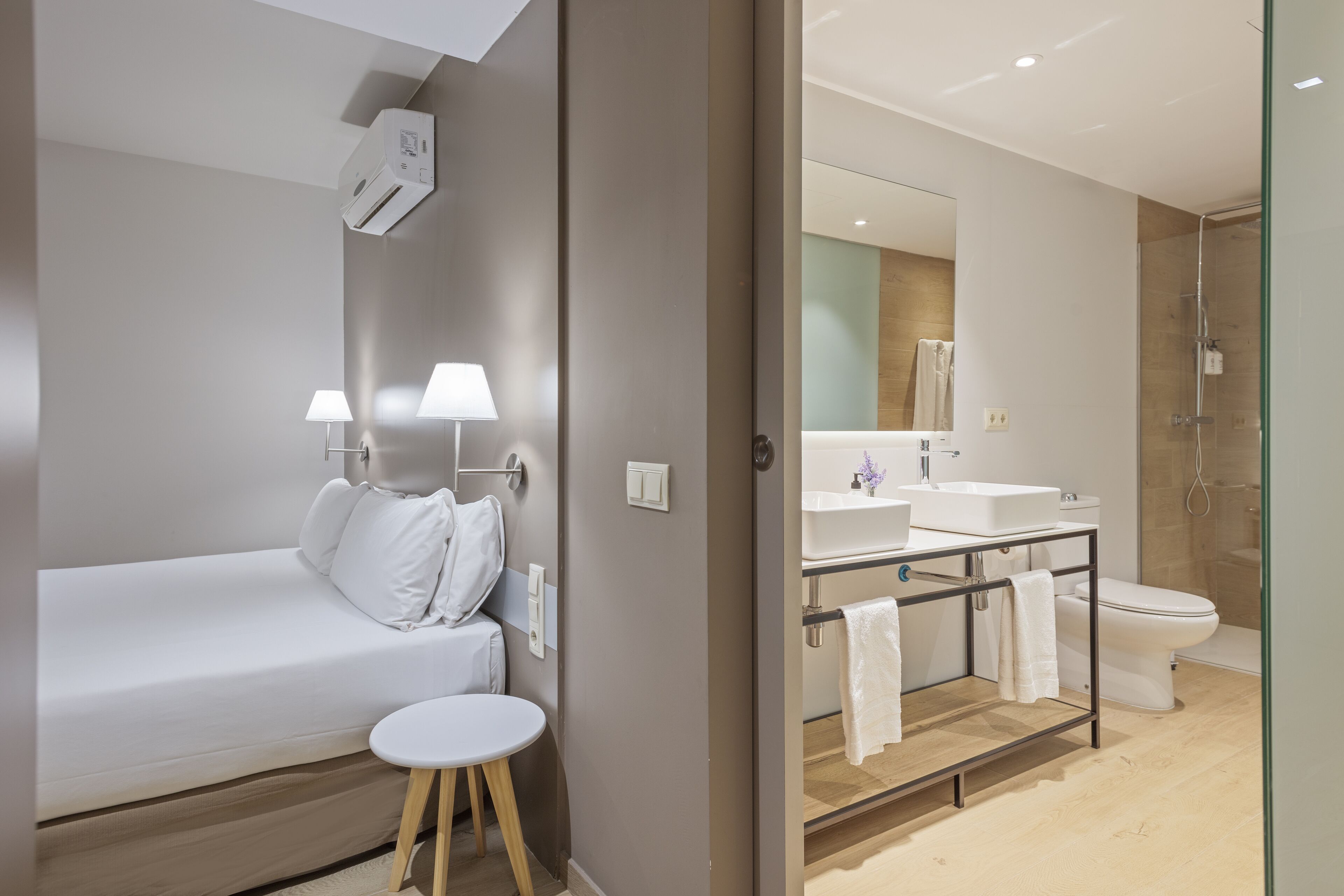 A modern hotel room with a bed, bedside lamps, a small round table, a bathroom with a shower, a sink, and a toilet.