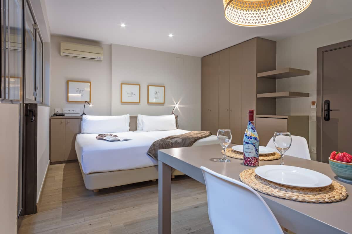 A modern hotel room with a bed, bedside table, and a dining area with a table and chairs.