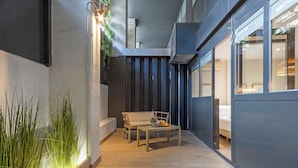 Un pasillo estrecho con suelo de madera, un banco y una mesa con frutas. A la derecha, una ventana y una pared con líneas verticales.