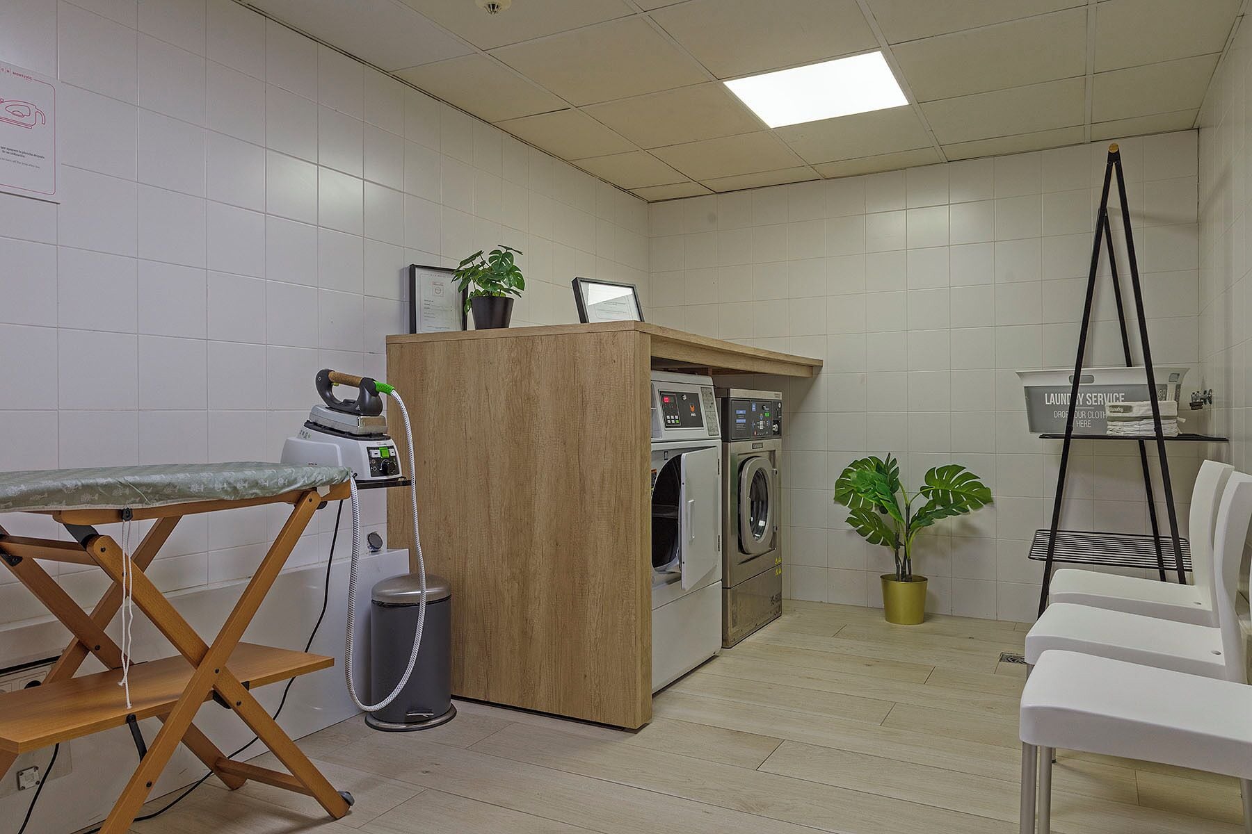 Ein kleiner Hauswirtschaftsraum mit Holz-Bügelstation, Waschmaschine, Trockner und Mülleimer.
