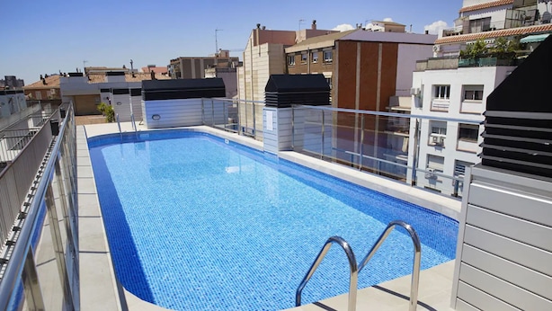 Una piscina en la azotea con superficie de agua azul cristalina, rodeada por una barandilla metálica y una barrera de vidrio.