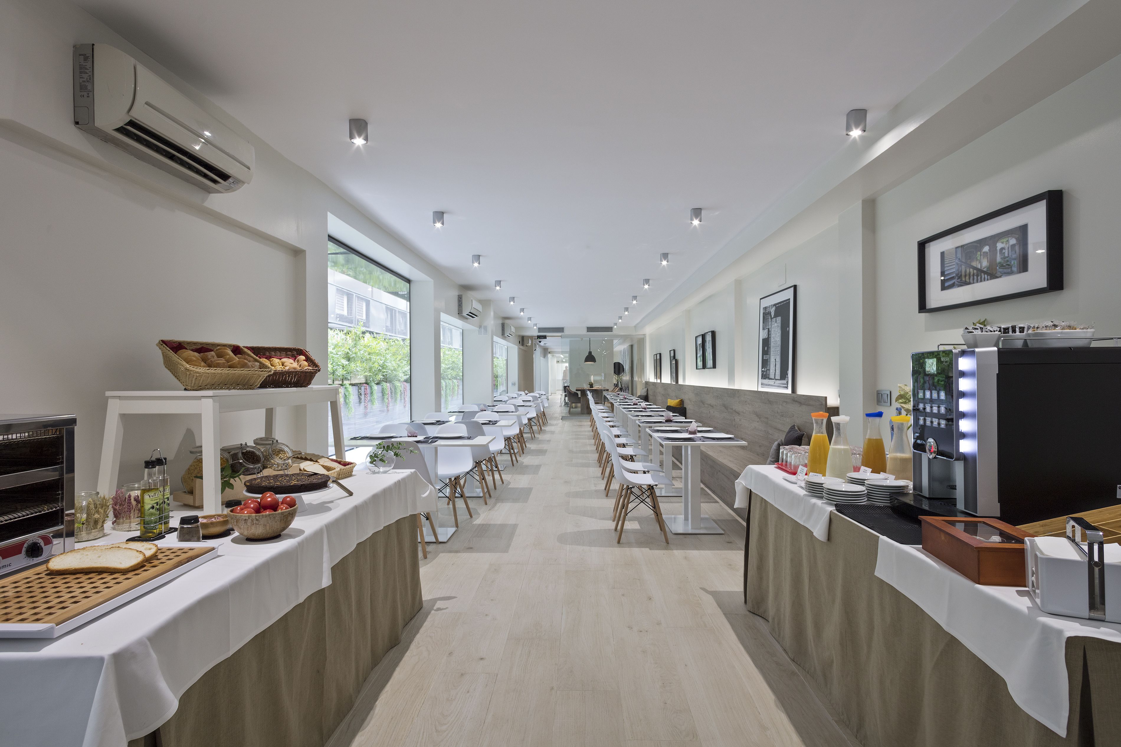 Ein langer Buffetstisch mit verschiedenen Speisen und einer Kaffeemaschine, platziert in einem hellen Raum mit großen Fenstern und modernem Design.