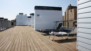 Une terrasse sur le toit avec un plancher en bois, des chaises longues et un bâtiment blanc doté d’un toit noir.