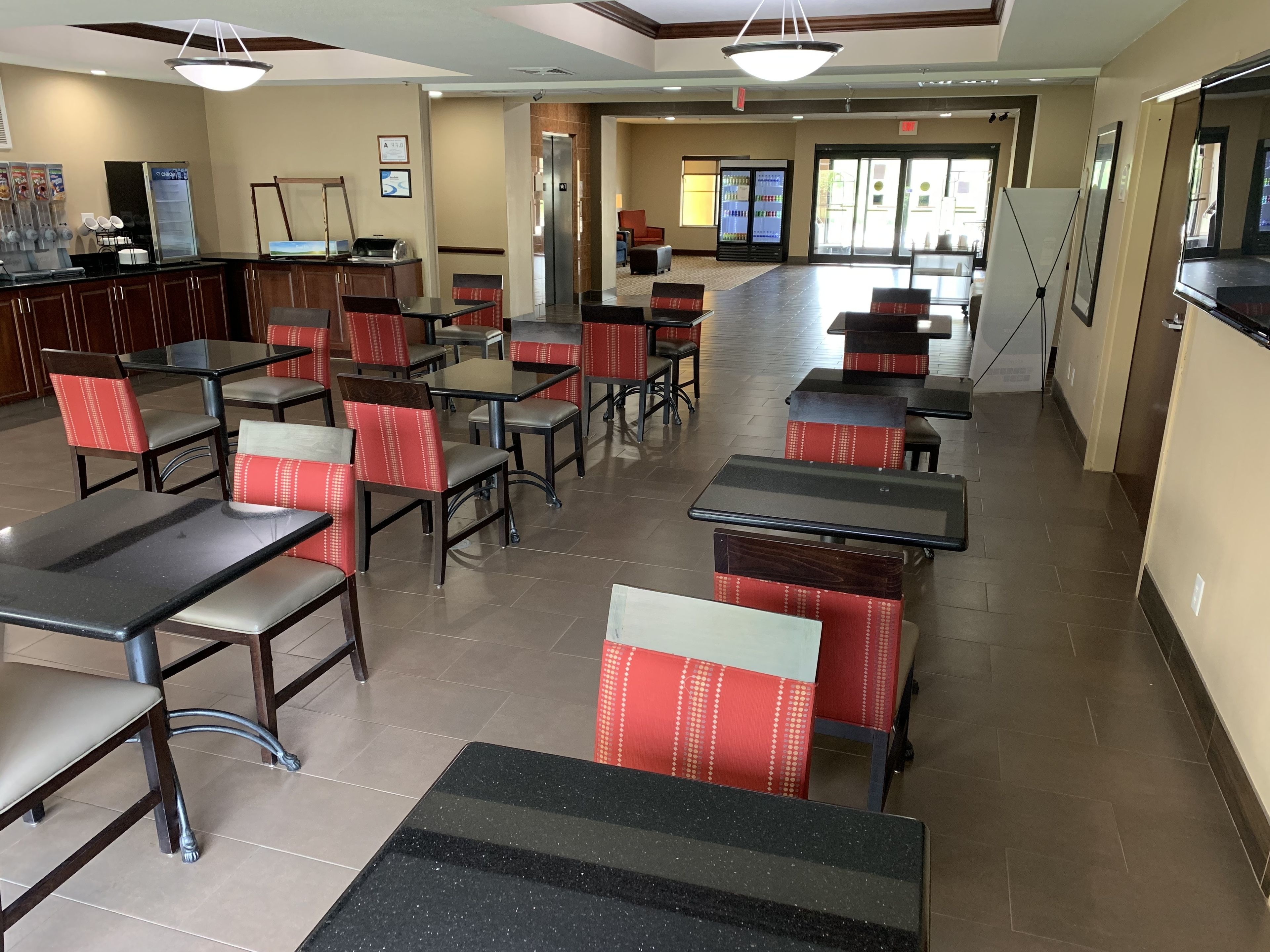 A spacious cafeteria with multiple tables and chairs, a refrigerator, and a vending machine.