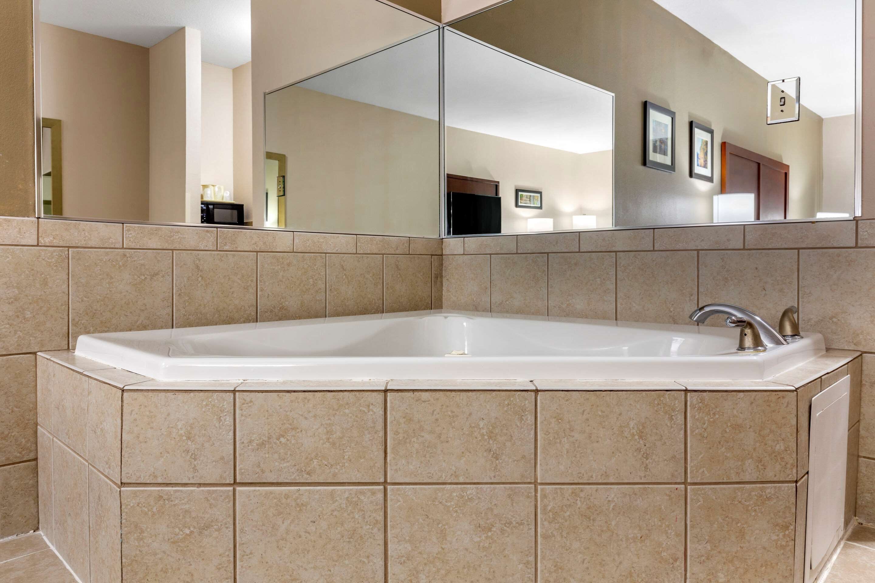 A large, rectangular bathtub with a modern faucet, set against beige tiled walls.