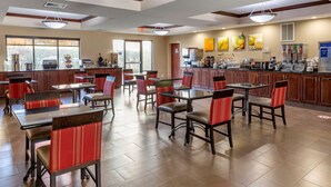 Un grand espace dédié à la salle à manger, avec plusieurs tables et chaises, un coin cuisine équipé de divers appareils et de grandes fenêtres laissant entrer la lumière naturelle.
