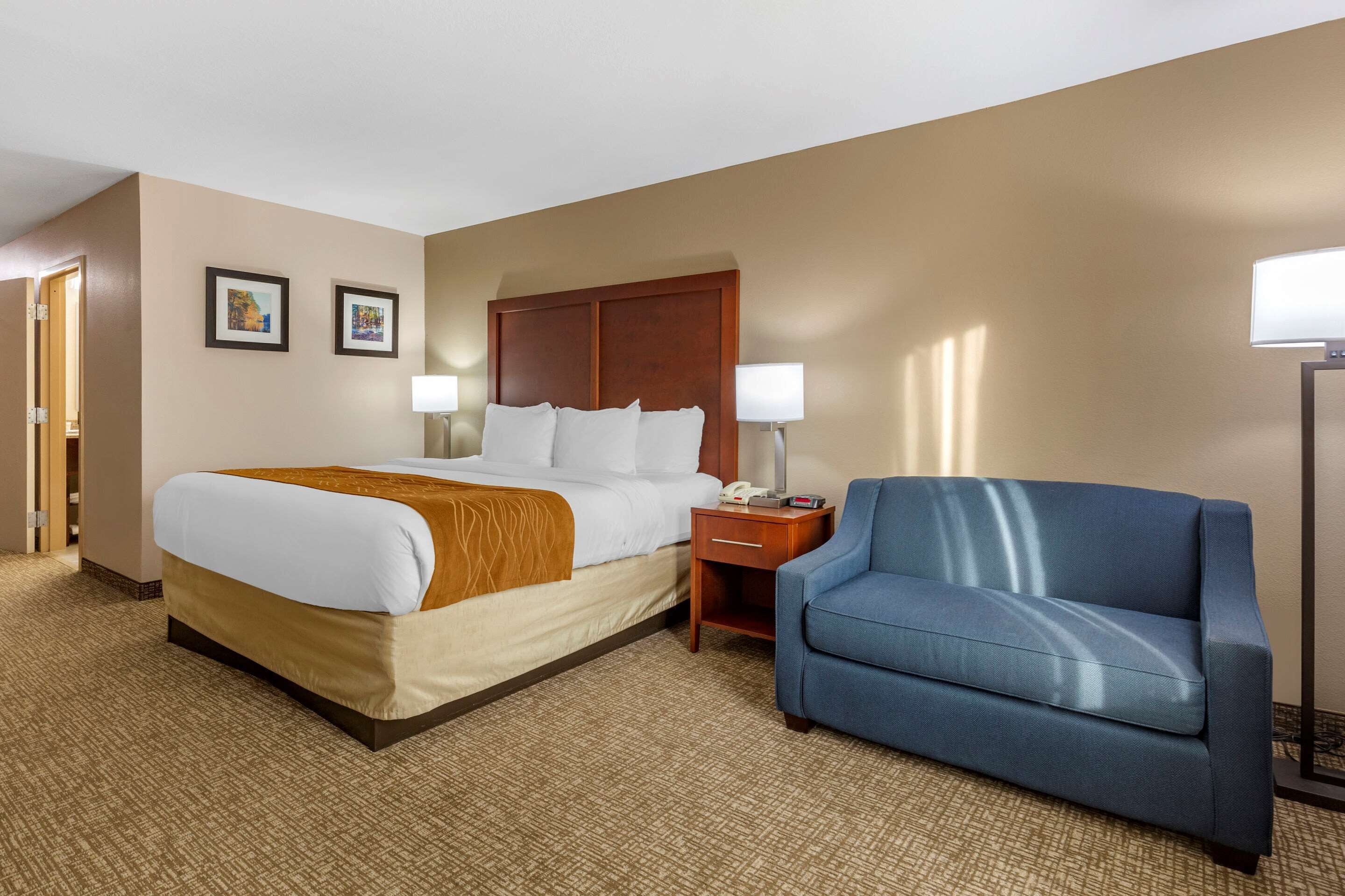 A hotel room with a large bed, a blue armchair, two bedside lamps, and a wooden headboard.