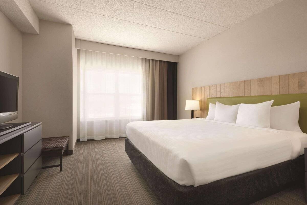 A hotel room with a large bed, a television, a desk, and a window with curtains.