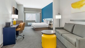A modern hotel room with a bed, a desk, a sofa, and a yellow ottoman. - Comfort Suites Nacogdoches (Nacogdoches)