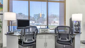 A modern office with two black mesh chairs, a desk with a computer and printer, and a large window with a view of a street and buildings.