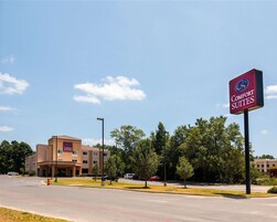 Un hotel Comfort Suites con cielo despejado, estacionamiento y un edificio con múltiples ventanas.