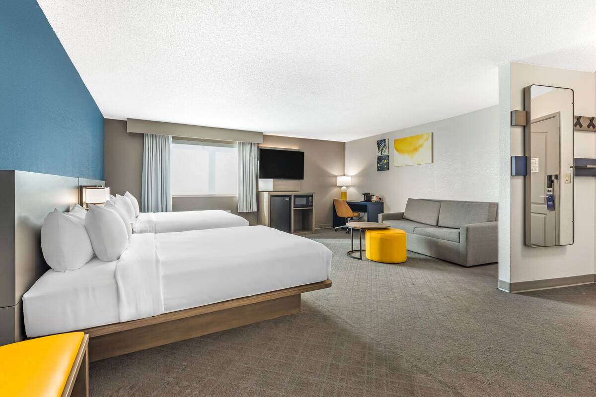 A hotel room with a large bed, a desk, a sofa, and a TV.