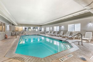 Una piscina interior con agua azul cristalina, rodeada de sillones blancos y suelo de baldosas.
