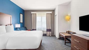 Une chambre d’hôtel avec un grand lit, un bureau, une chaise, une télévision et une fenêtre avec des rideaux.