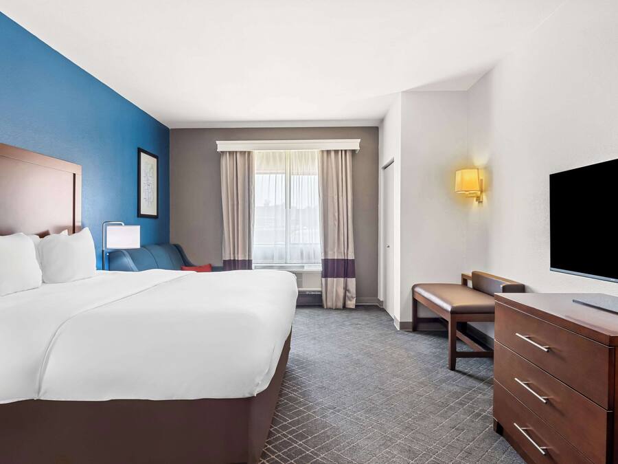 Une chambre d’hôtel avec un grand lit, un bureau, une chaise, une télévision et une fenêtre avec des rideaux.
