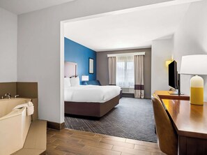 A hotel room with a bed, a desk, a chair, a bathroom with a bathtub, and a window with curtains.