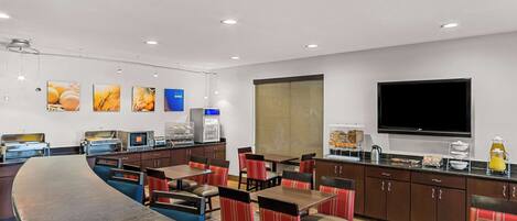 A modern hotel restaurant with a long counter, multiple seating areas, and a large flat-screen TV.