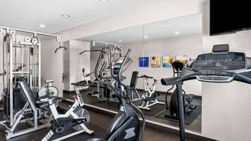 A gym with various exercise machines, a mirrored wall, and a television screen.