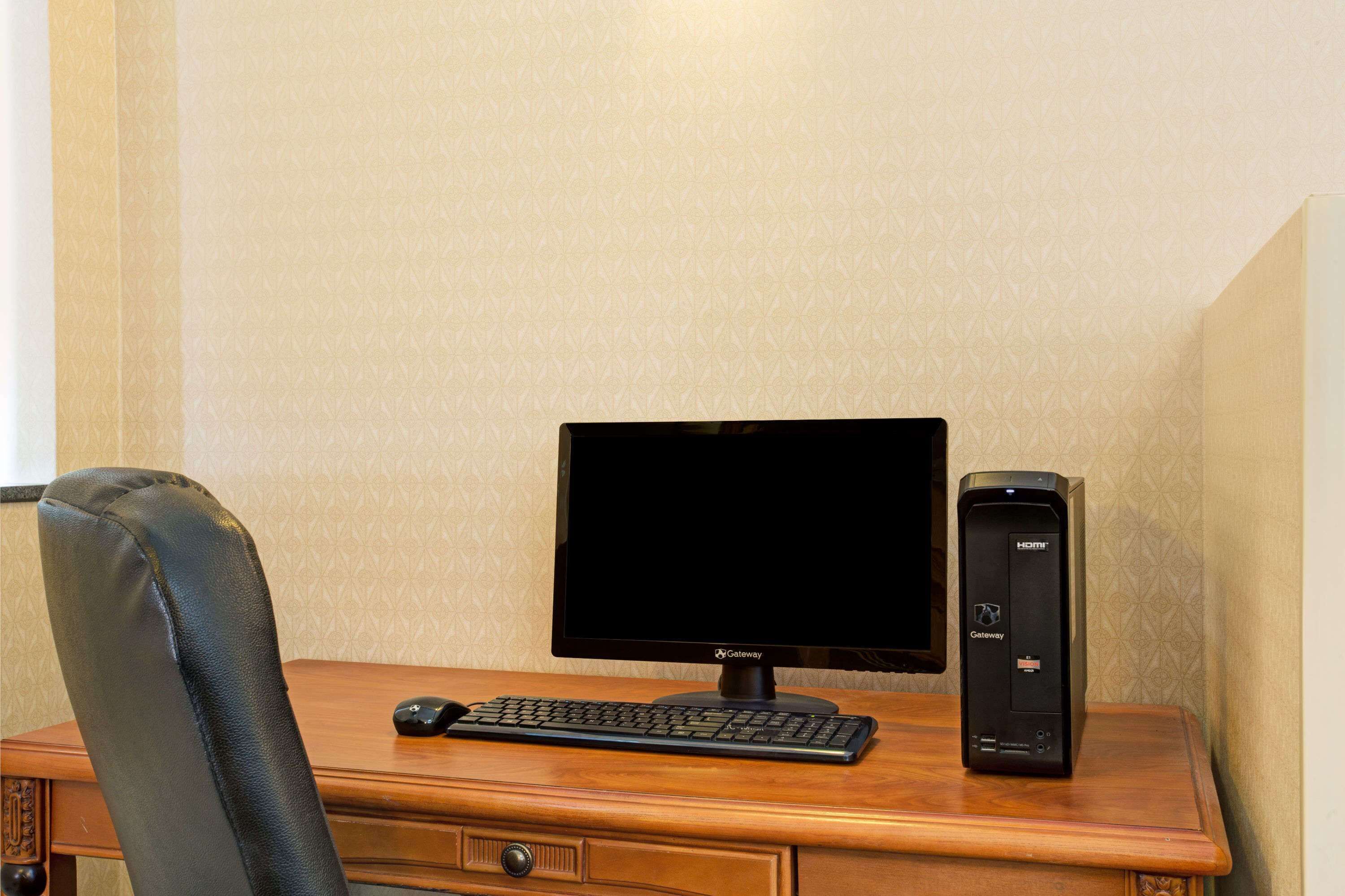 Un escritorio de madera con un monitor negro Gateway, un teclado negro y un ordenador de sobremesa negro.
