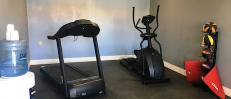 A home gym with a treadmill, elliptical, and a water dispenser.