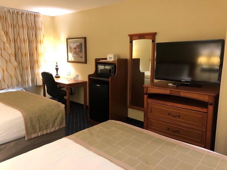 Habitación de hotel con dos camas, un escritorio con computadora, microondas, televisión y espejo.