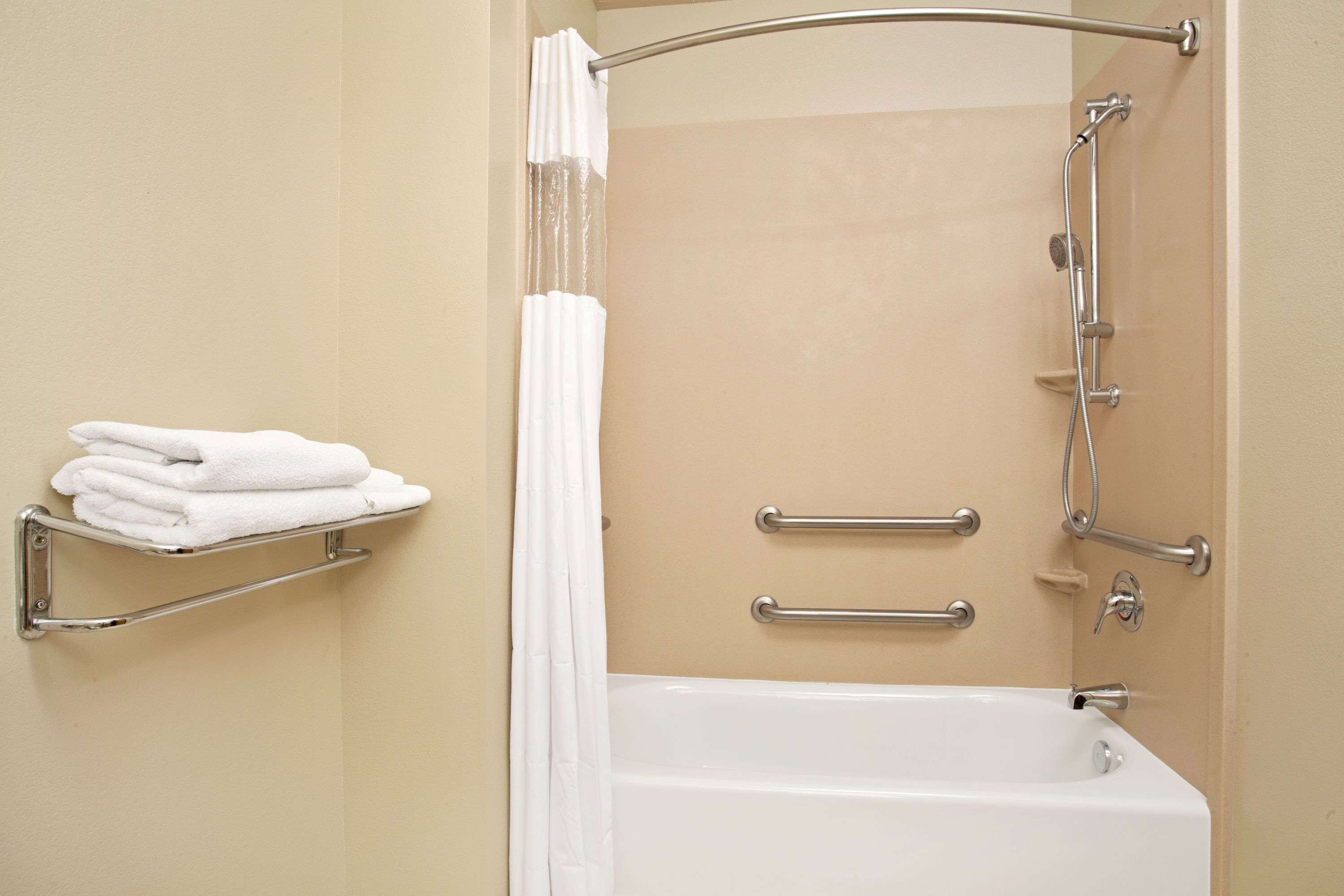 A bathroom with a bathtub, a towel rack with folded towels, a shower curtain, and grab bars.