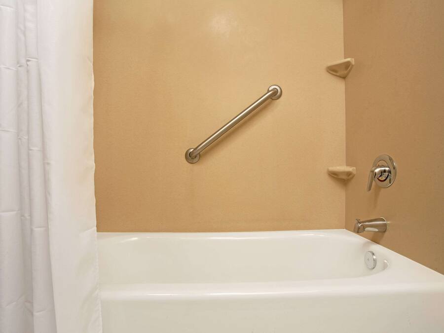 Une salle de bain avec une baignoire blanche, un mur de couleur beige et une barre d’appui fixée au mur.