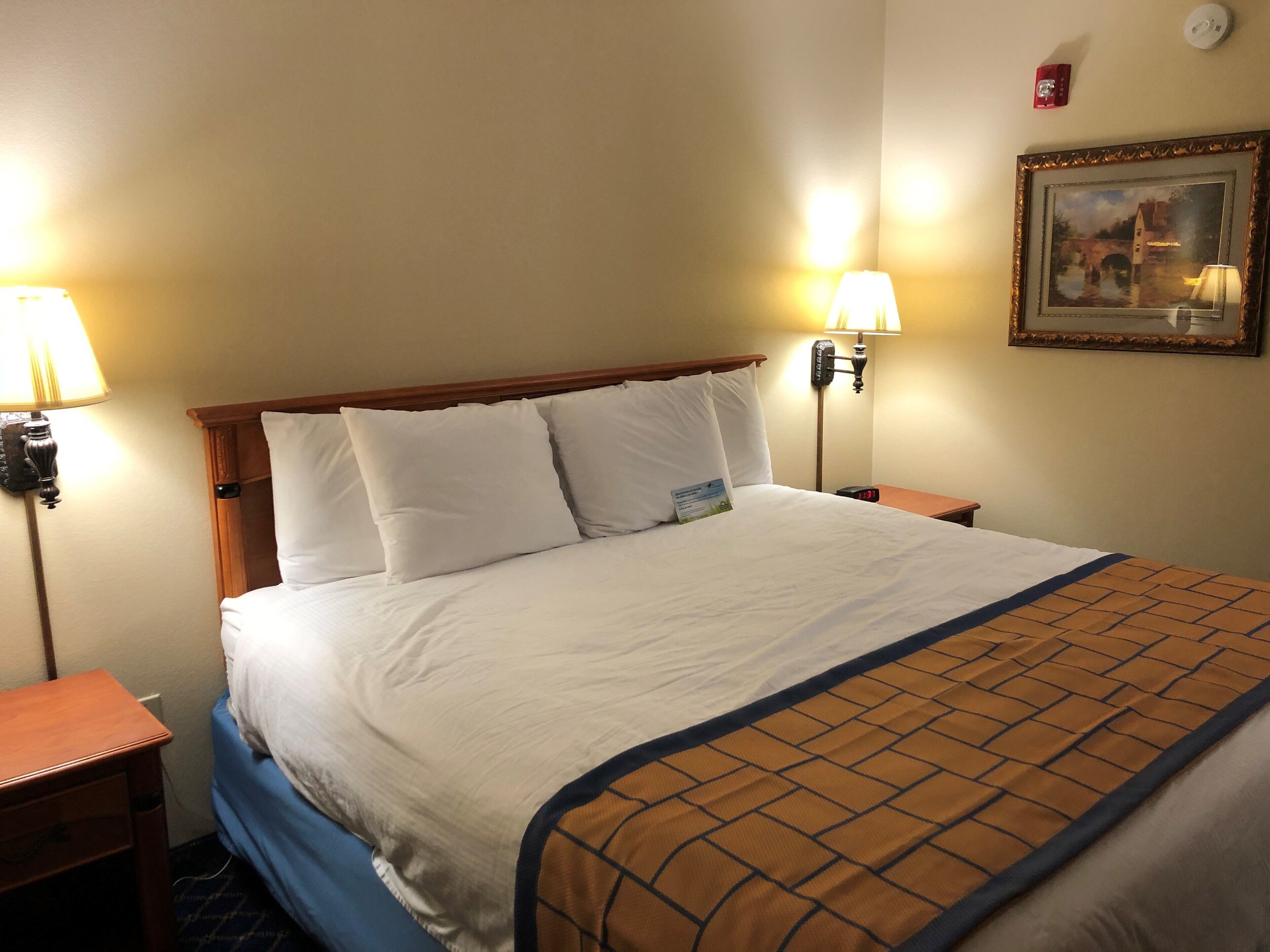 Una habitación de hotel con una cama grande, dos lámparas de noche, una mesita de noche, un cuadro en la pared y una luz de emergencia roja.