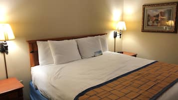 Una habitación de hotel con una cama grande, dos lámparas de noche, una mesita de noche, un cuadro en la pared y una luz de emergencia roja.