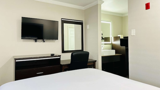 Habitación de hotel con cama, escritorio, silla, televisor y baño con lavamanos.