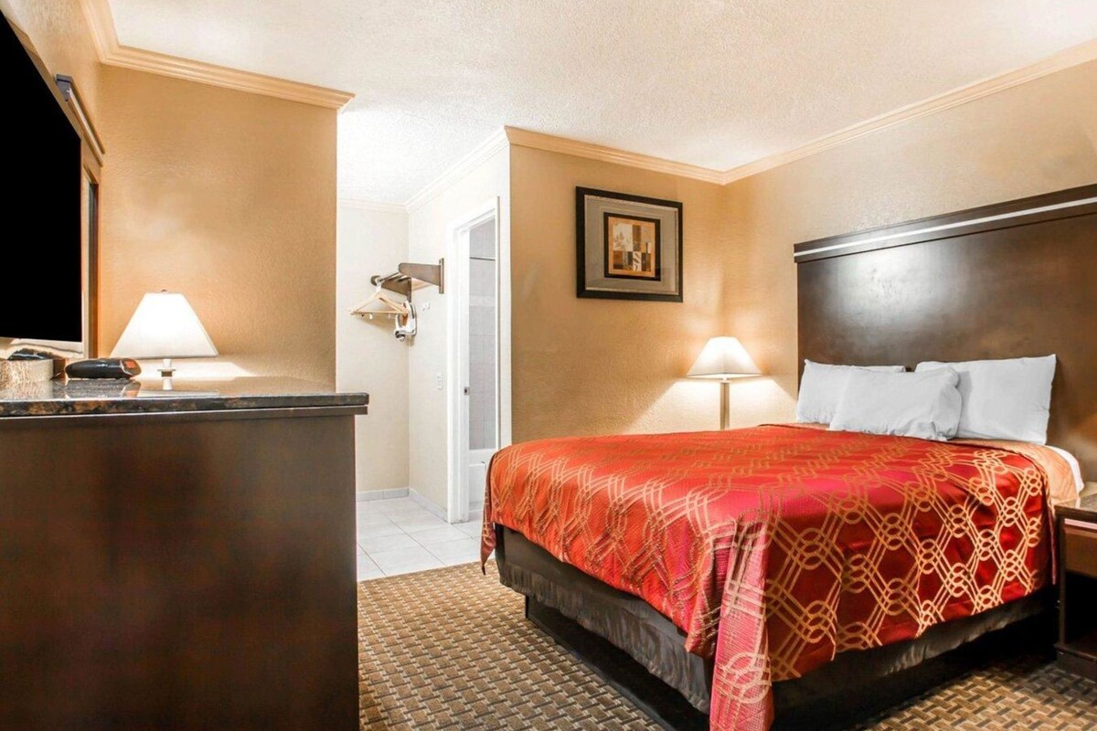 A hotel room with a bed, bedside lamps, a desk, and a door.