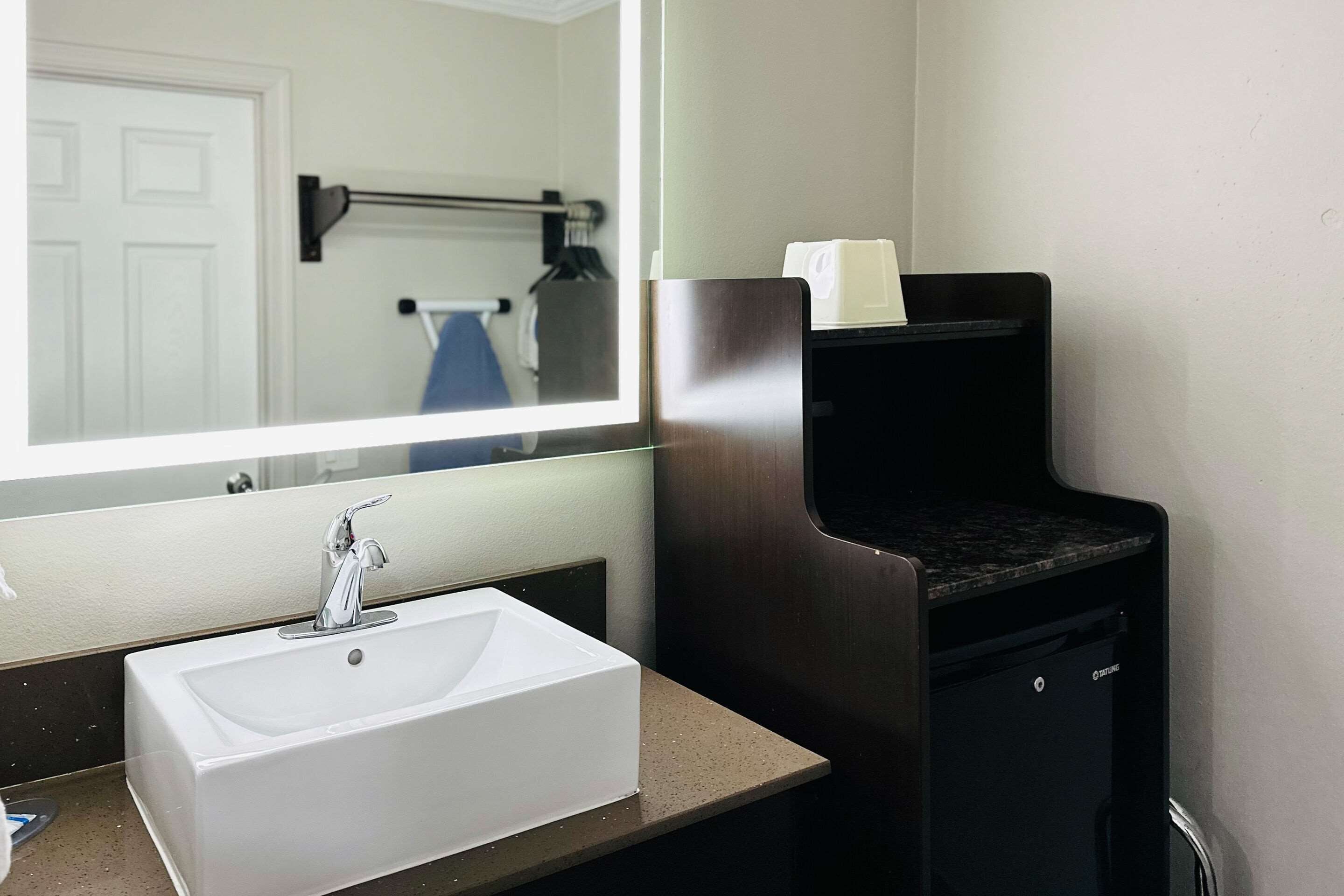 A bathroom with a white sink, a mirror, and a black trash bin.
