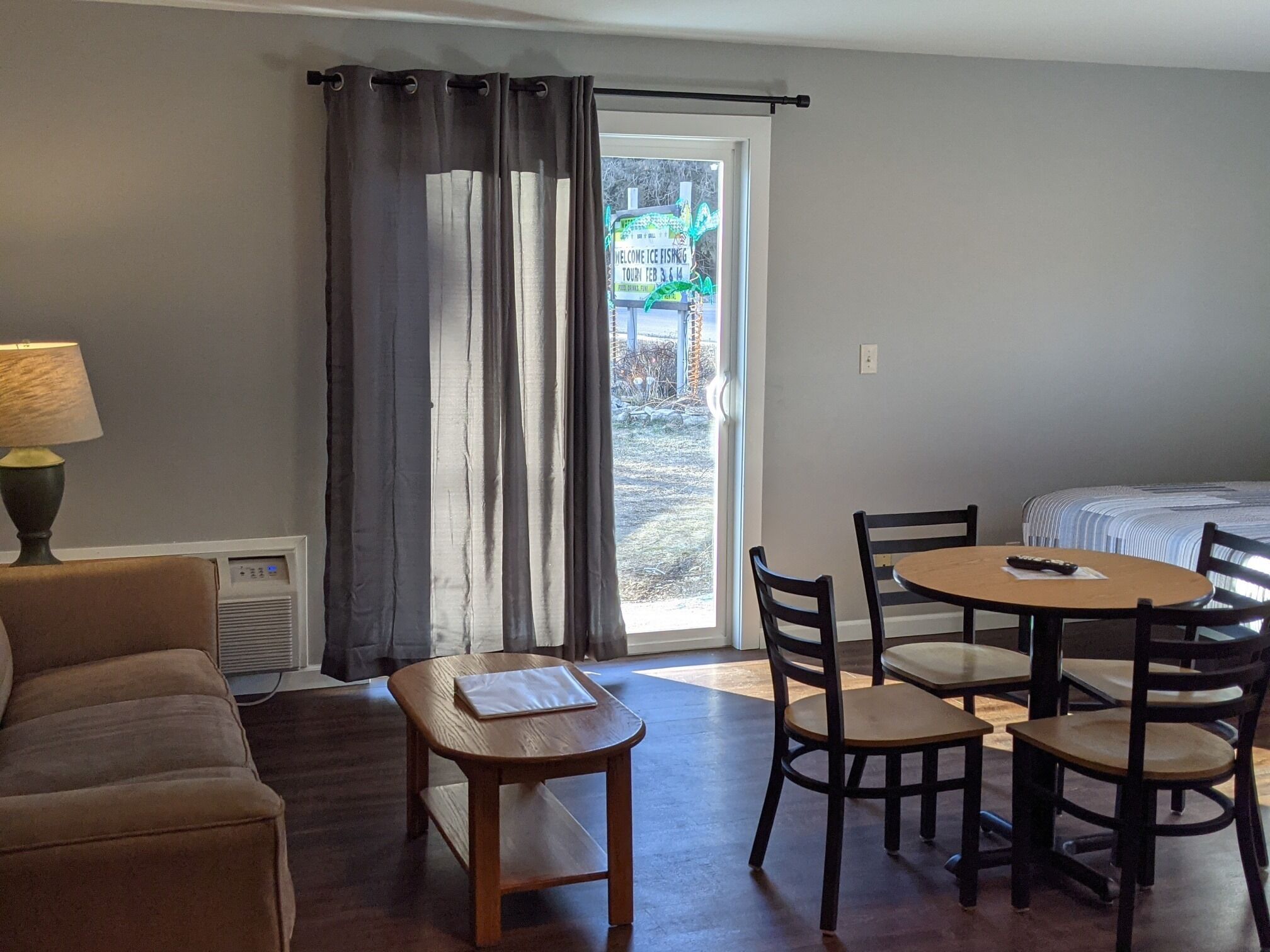 A room with a sofa, a small table, a round dining table with chairs, a bed, and a window with curtains.
