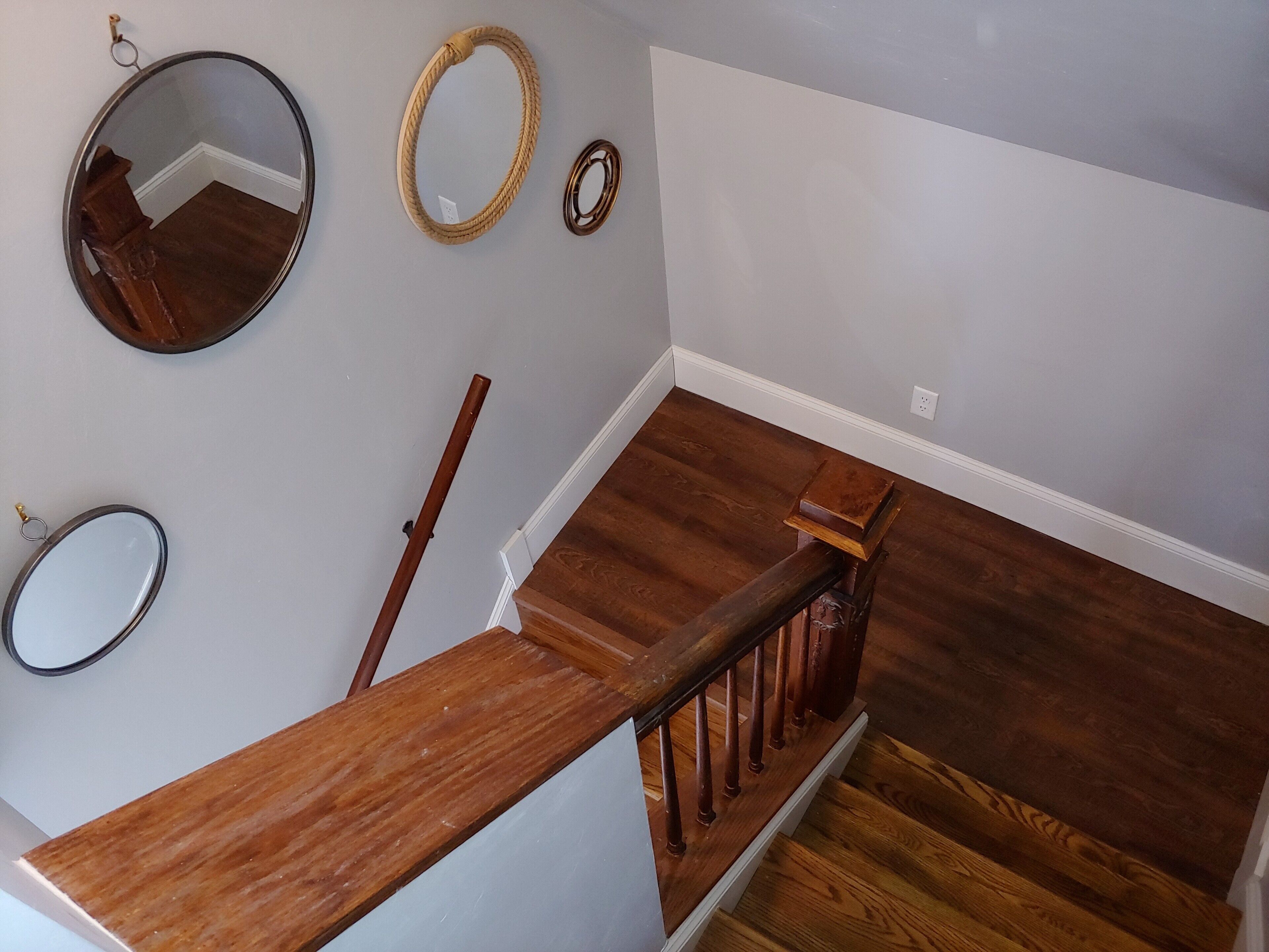A wooden staircase with a handrail, a wooden bench, and three wall-mounted mirrors.