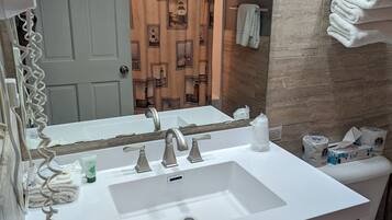 A bathroom with a white sink, two faucets, a mirror, and a towel rack with folded towels.