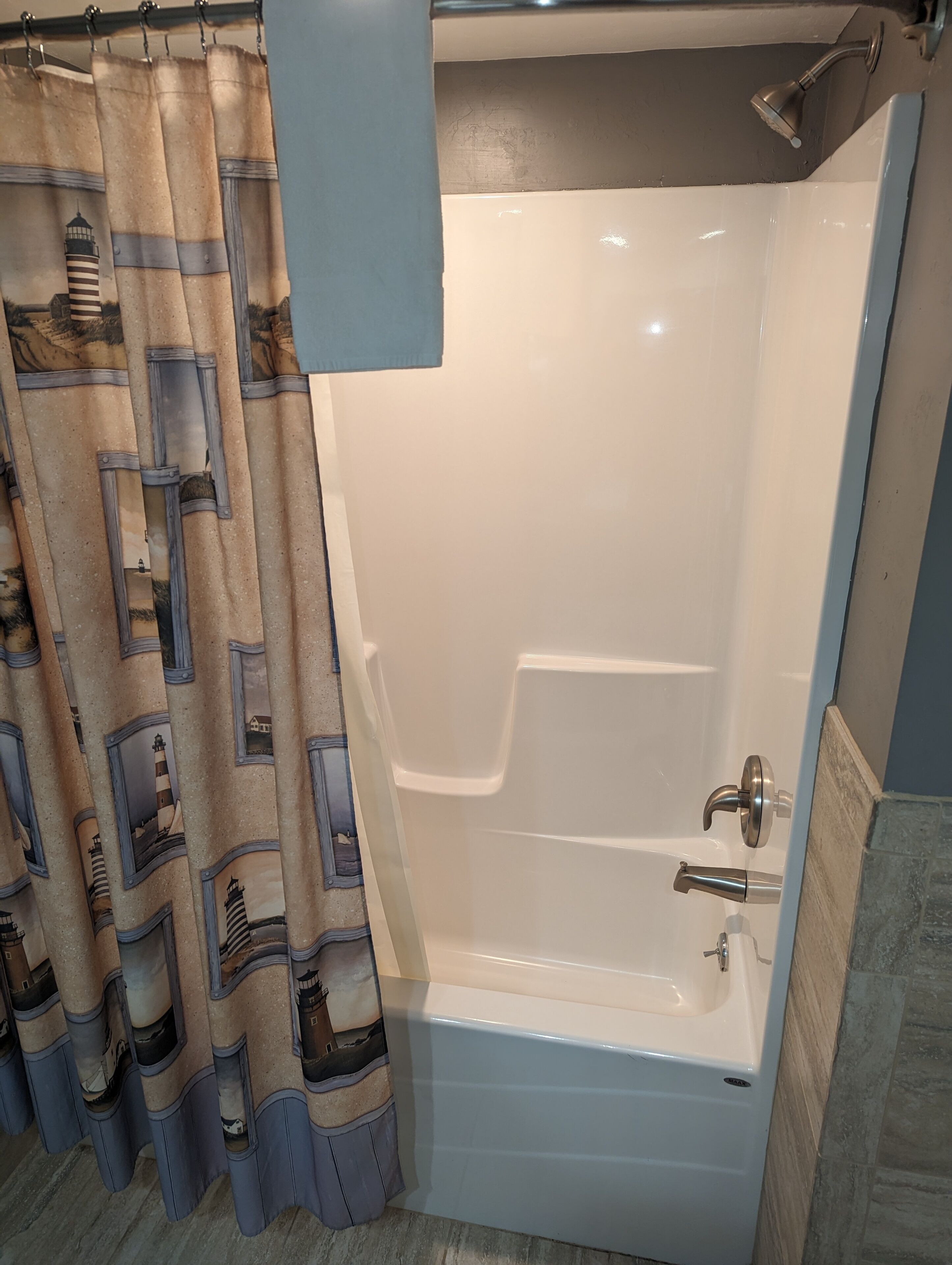 A bathroom with a bathtub, a shower, and a curtain with a lighthouse design.