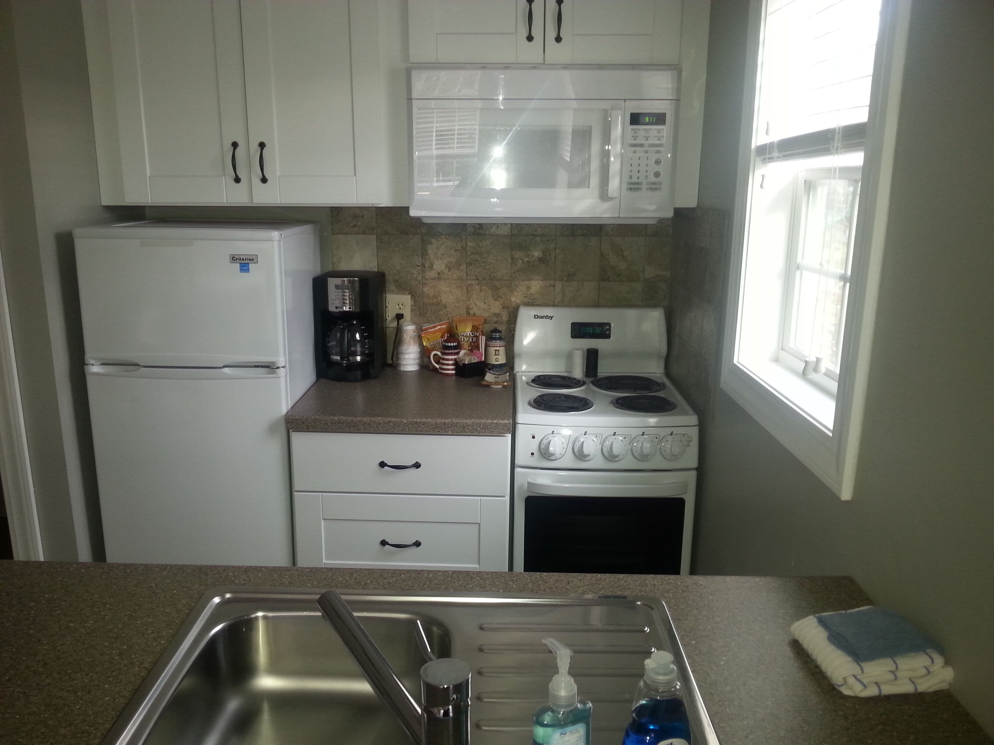 A kitchen with white cabinets, a refrigerator, a microwave, a stove, and a sink with soap dispensers.